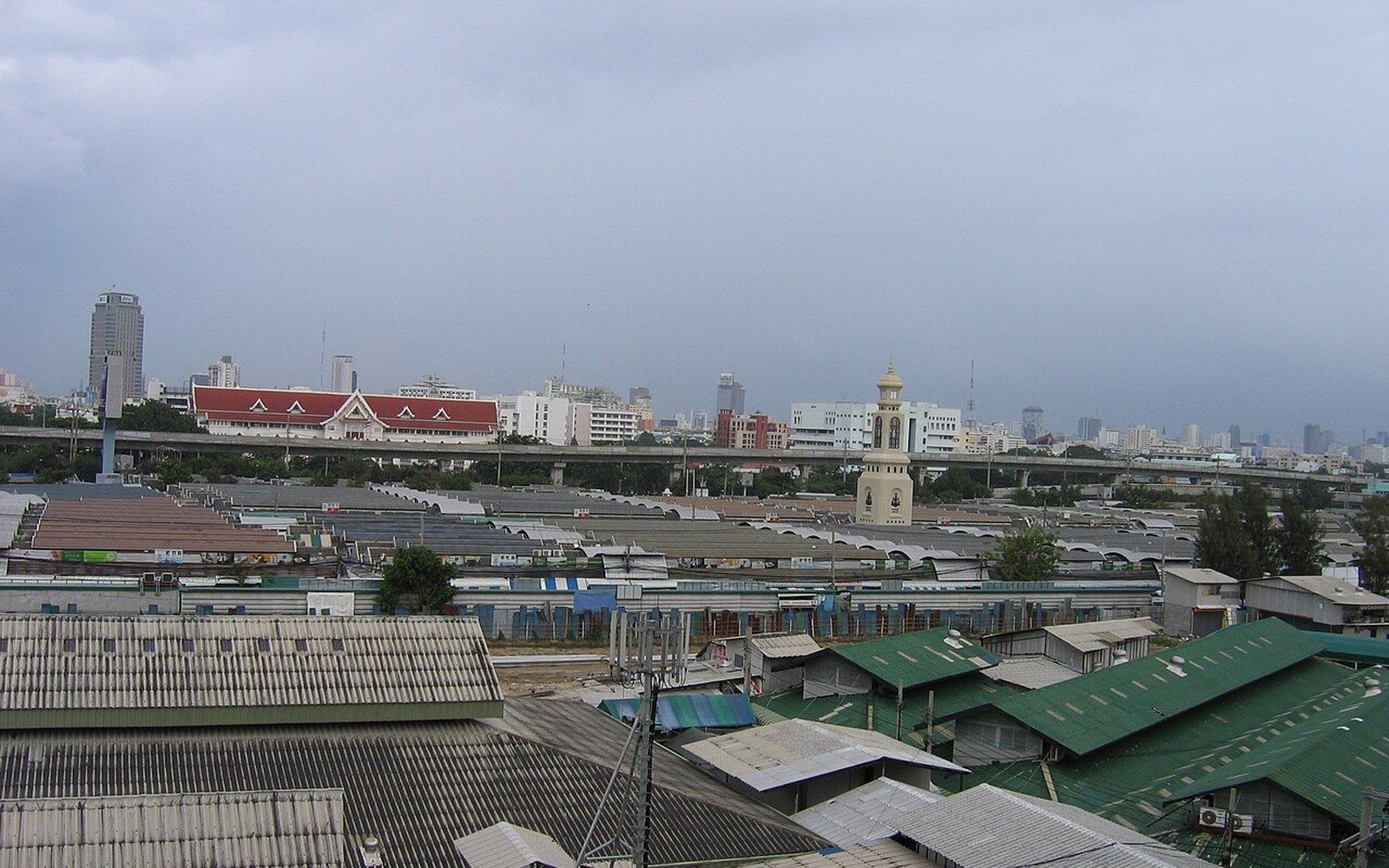 Rows of market rooftops stretch toward a distant city skyline under overcast skies