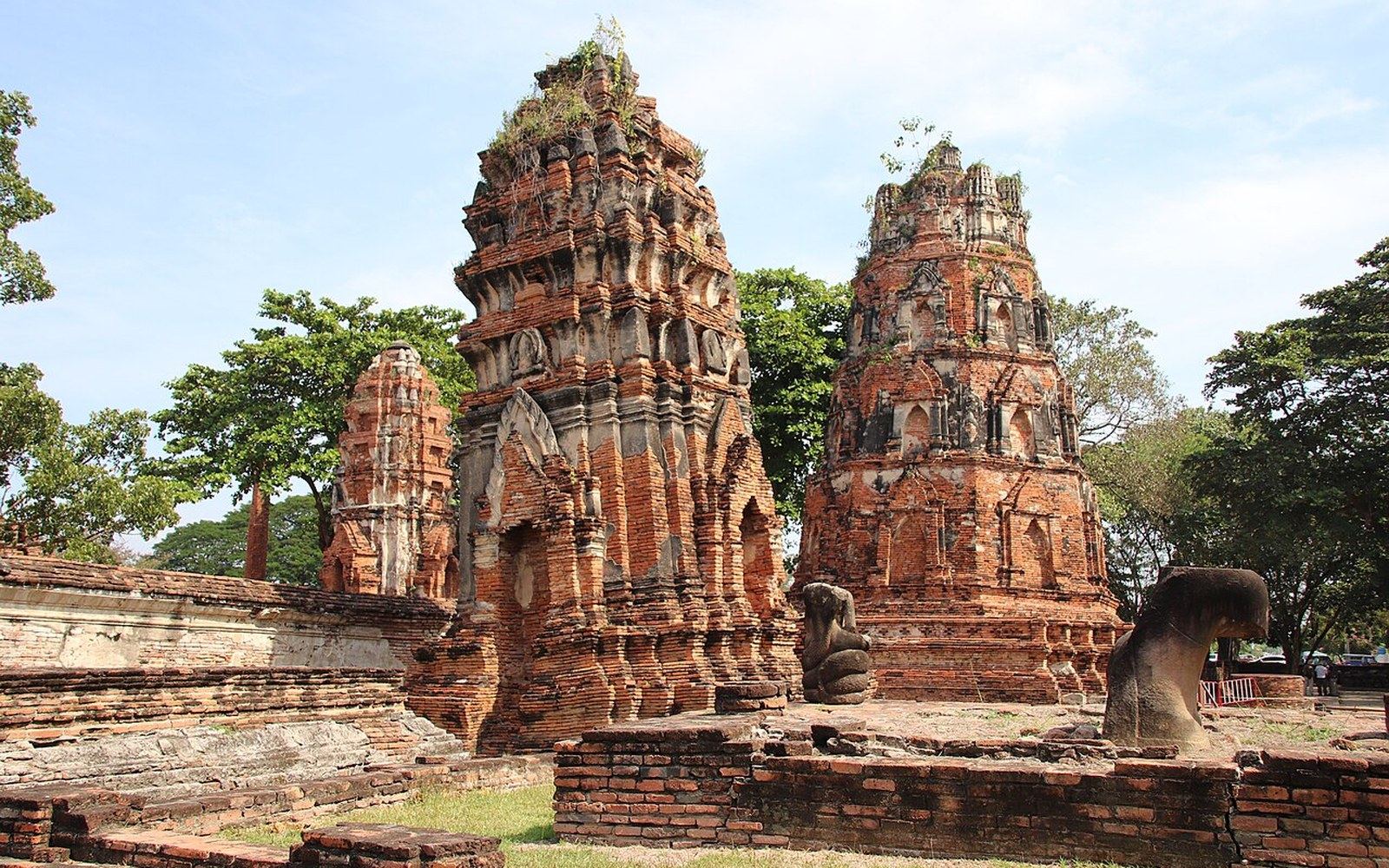 Weathered brick prangs with vegetation growing atop ancient temple ruins in Ayutthaya